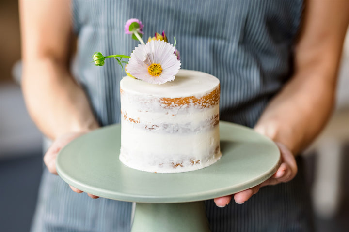 A person holding a small chocolate cake with a flower crown.