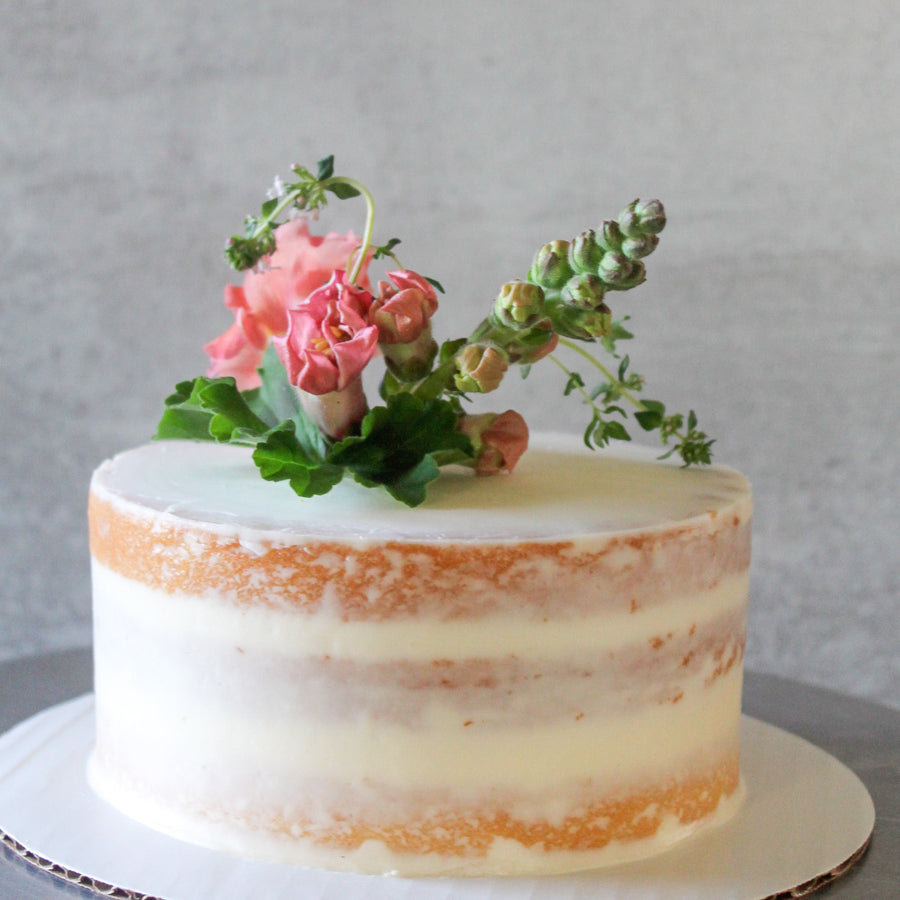 A round cake covered in a sheer layer of white buttercream and decorated with a bouquet of fresh flowers and greenery on top.