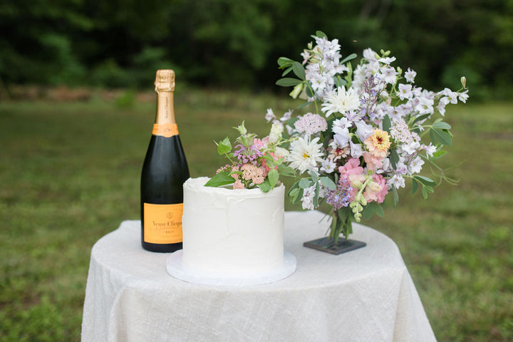 A cake decorated with a plume of pastel-toned flowers beside a bouquet of the same.