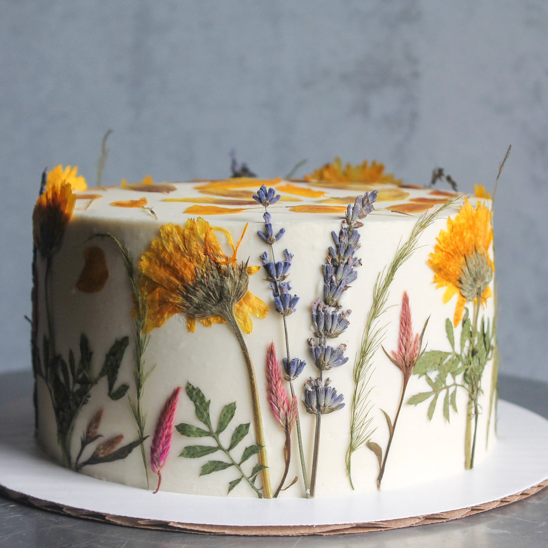 A cake frosted with smooth, white buttercream and decorated all over with pressed flowers.