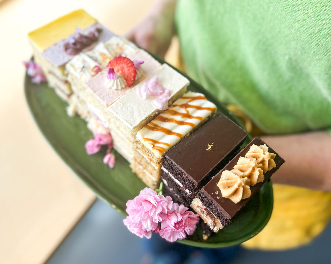 A person holding a ceramic platter with eight slices of cake, each a different flavor.