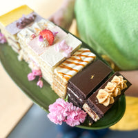 A person holding a ceramic platter with eight slices of cake, each a different flavor.