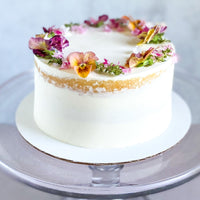 A round cake frosted in a sheer layer of white buttercream and decorated with a fresh floral crown.