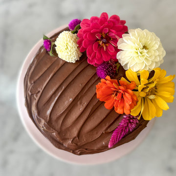 A round cake frosted with fudgey buttercream and decorated with a crescent of fresh flowers.