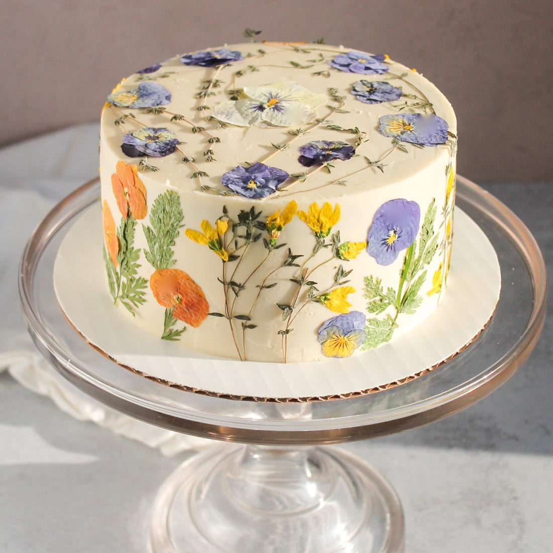 A cake frosted with smooth, white buttercream and decorated all over with pressed flowers.