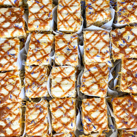 Top-down view of several square carrot cake slices, each wrapped in parchment paper.