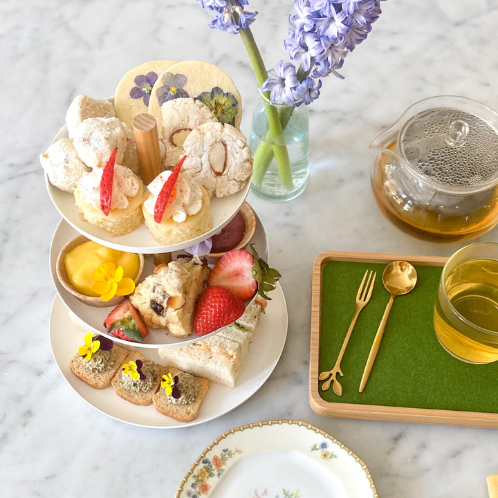 A tea tower with scones, tea sandwiches, fruit, curd, and cookies, all beside a pot of tea.