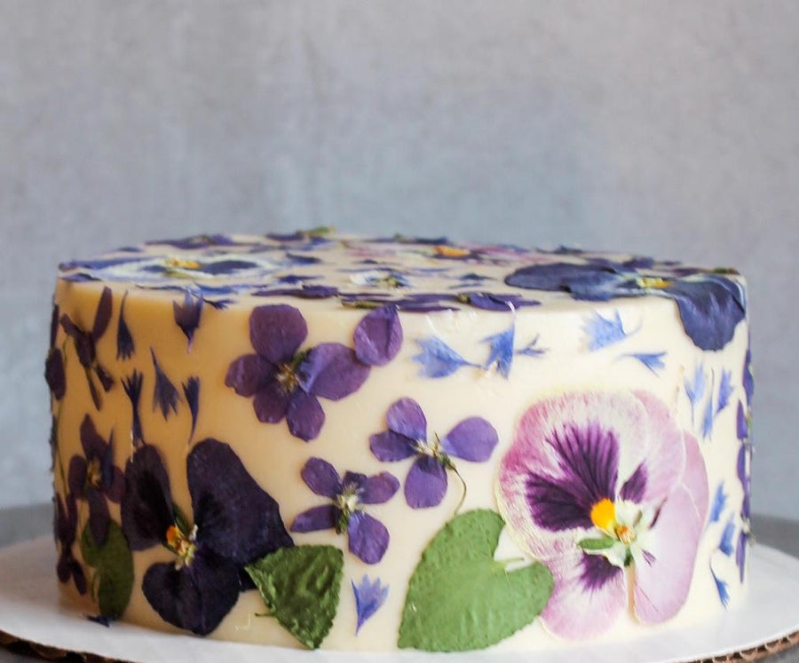 A cake frosted with smooth, white buttercream and decorated all over with pressed flowers.