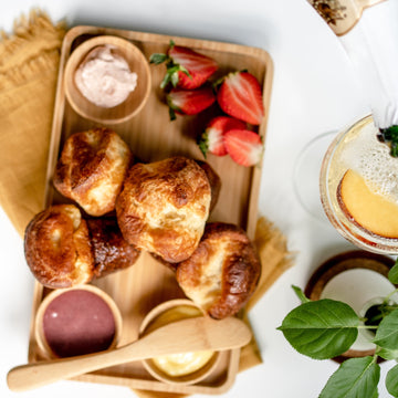 A platter containing fresh popovers, various house-made sauces and butters, and a garnish of sliced strawberries.