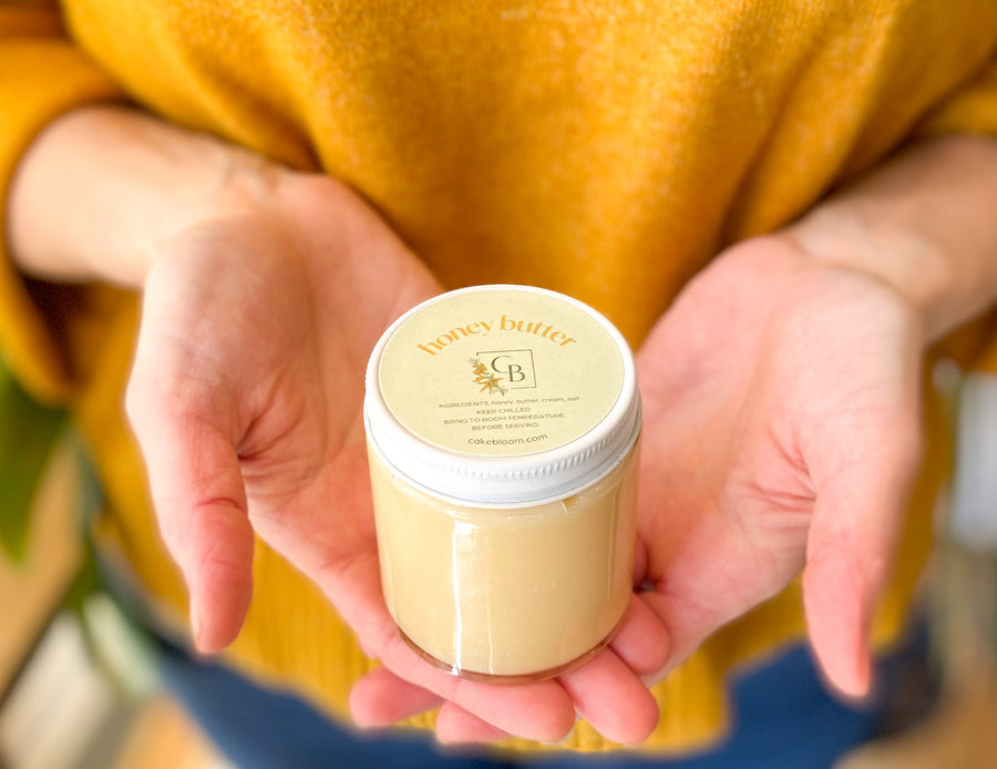 A person holding a jar of honey butter in cupped hands.