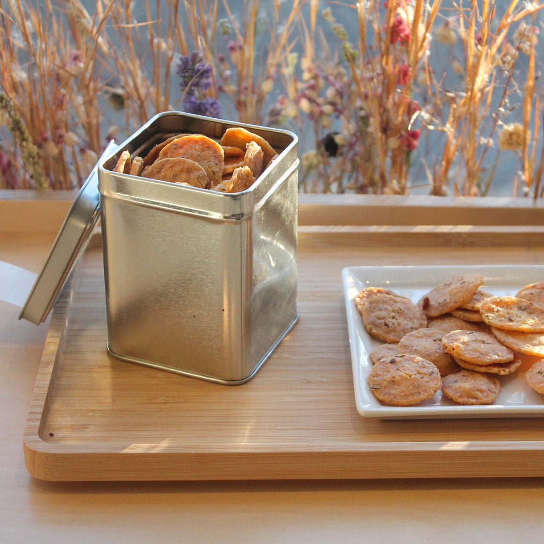 A plate of spicy cheese coins, placed beside an open metal canister of the same.